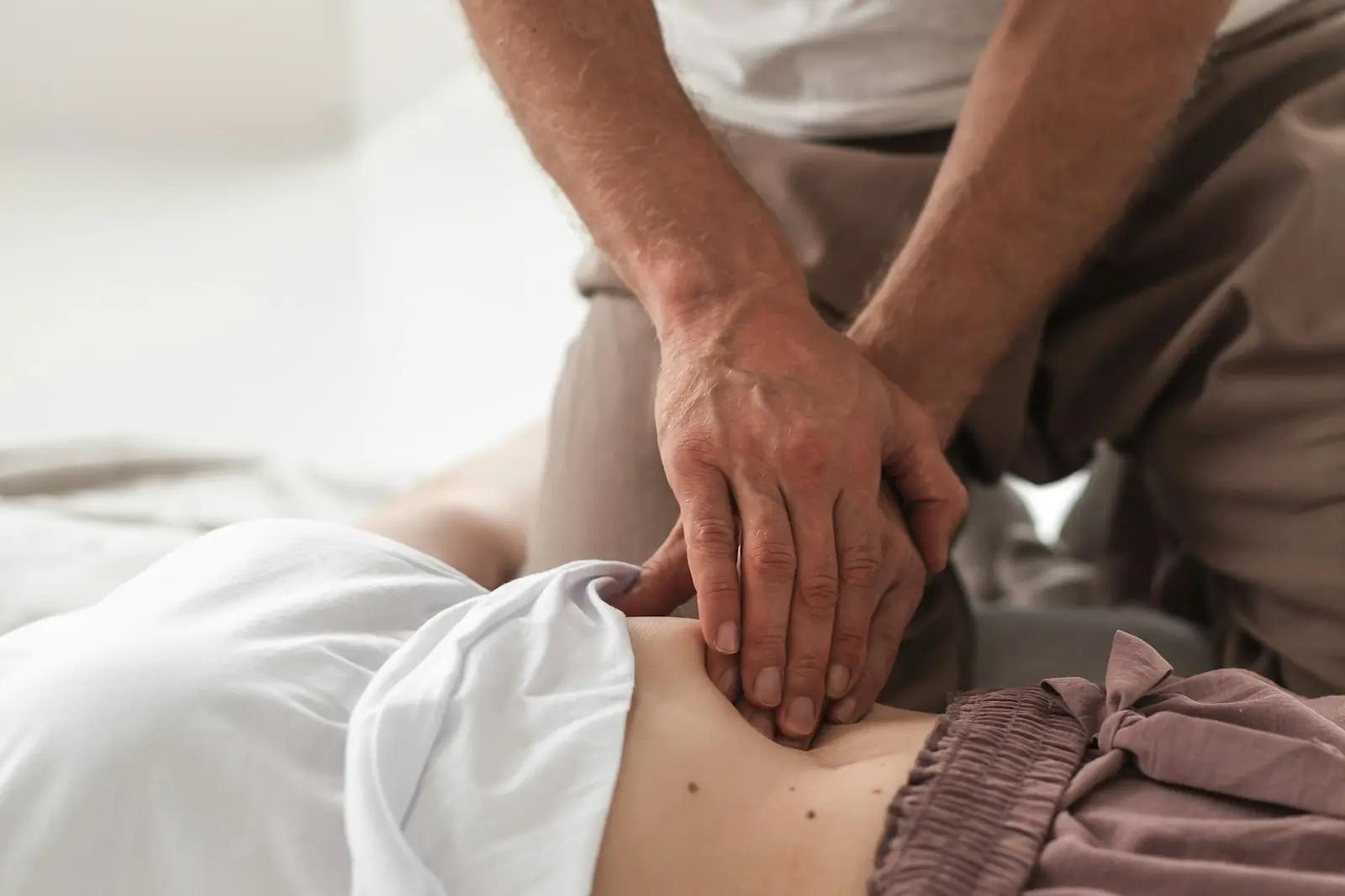 Osteopat som behandler magen og hoften til en pasient med hendene