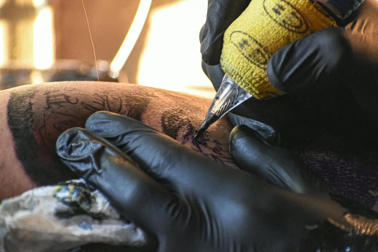 Tatovør med svarte hansker som tatoverer en arm med tatoveringsmaskin